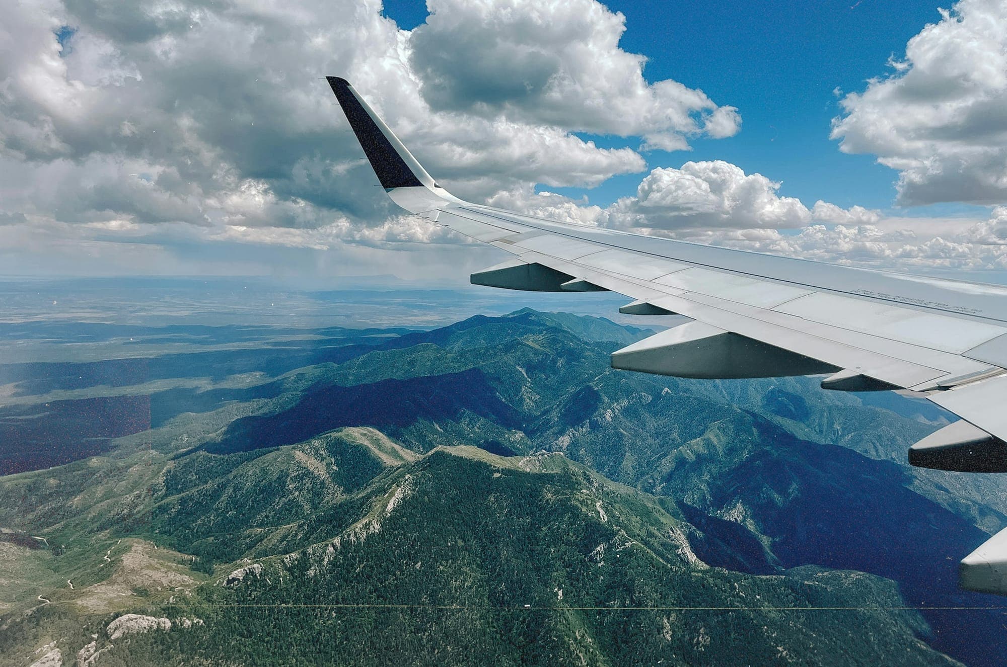 An aircraft wing over a green mountain range, seen from the cabin window